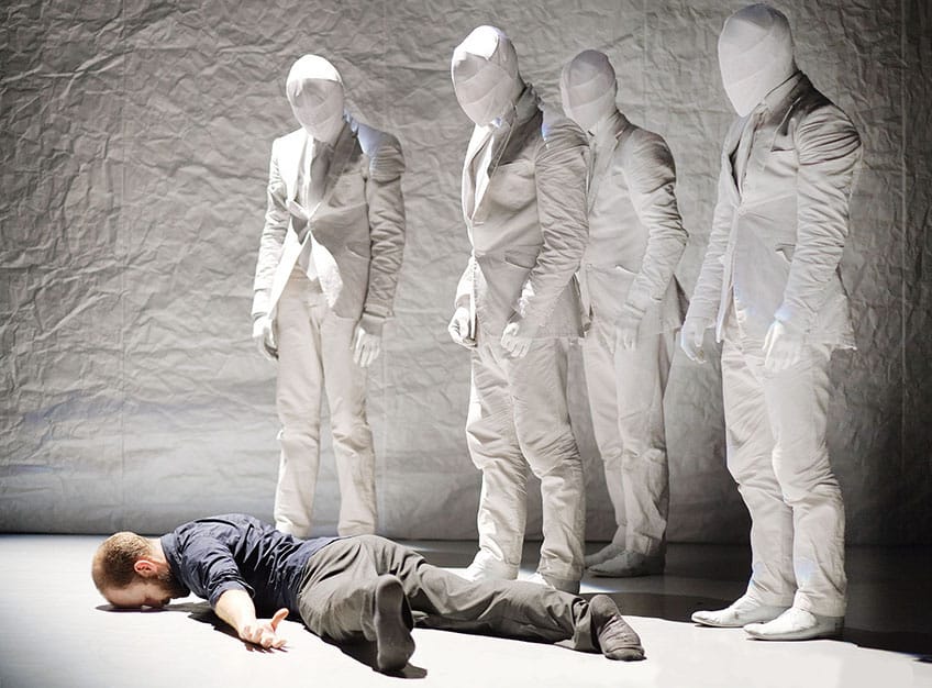 Man lying on ground next to five corporate mummies