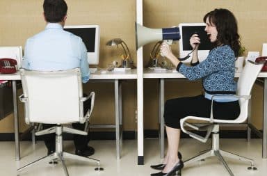 Woman yelling at man using a bullhorn at work desks