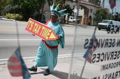 Tax man wearing Statue of Liberty costume with "Tax Time" sign