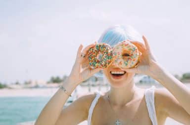 Portrait of a young woman laughing and covering eyes with donuts